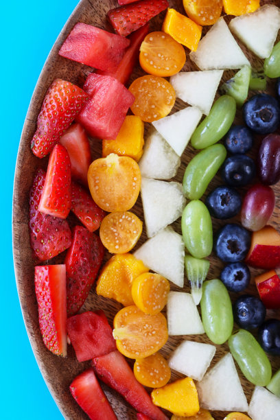 特写图片:五颜六色的水果，草莓，西瓜，芒果，树莓(印度覆盆子)，蜜瓜，白葡萄，猕猴桃，蓝莓，李子和红葡萄放在木制砧板上，蓝色背景，高架视图图片下载