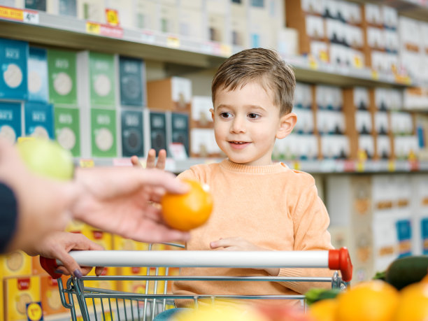 在超市里，男孩从父母手里接过一个新鲜水果图片下载