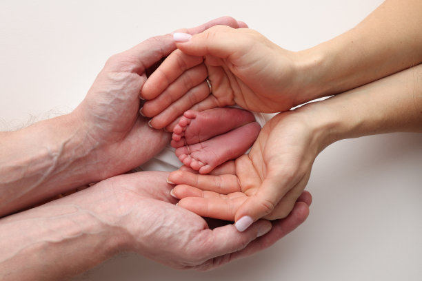 爸爸的手心，妈妈的脚上都抱着刚出生的婴儿的白毯子。新生儿的脚放在父母的手掌上。工作室微距照片的一个孩子的脚趾，脚跟和脚。图片下载