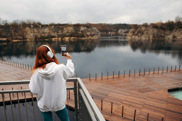 红头发的运动女孩戴着耳机，在克拉科夫的扎克佐韦克采石场的木制码头拍摄湖泊照片图片下载