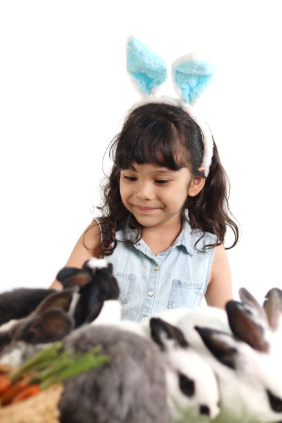 长着蓝色兔子耳朵的可爱小女孩在绿草地上和兔子玩耍。快乐的孩子被宠物包围着。在白色背景上庆祝复活节。快乐的孩子在复活节庆祝节日。图片下载