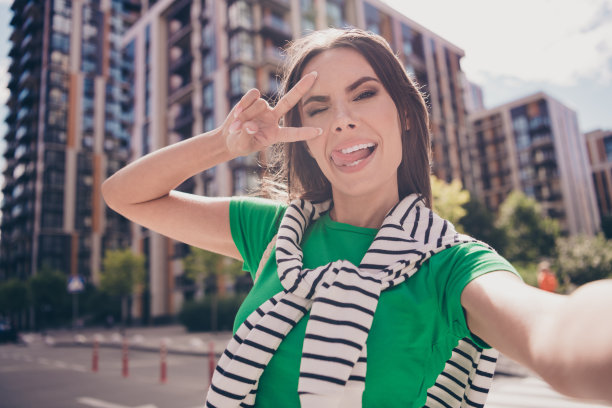 年轻时髦女友的自拍照片，露出v字，遮住脸，伸出舌头，享受周末户外街道住宅区图片下载