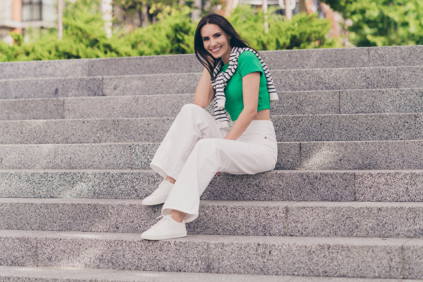 照片中的女孩穿着绿色的上衣，坐在楼梯上享受着城市公园外面温暖的阳光图片下载