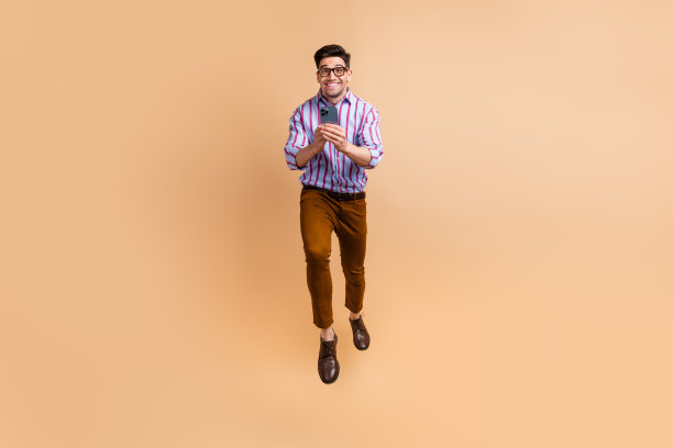疯狂时髦的男人穿着时尚的衣服，在空中飞行，写作打字短信评论帖子孤立的米色背景的全长照片图片下载