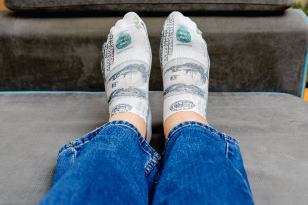 一个男人穿着蓝色牛仔裤躺在床上，袜子上印着一美元的图案。室内拍摄，选择性对焦，特写。图片下载