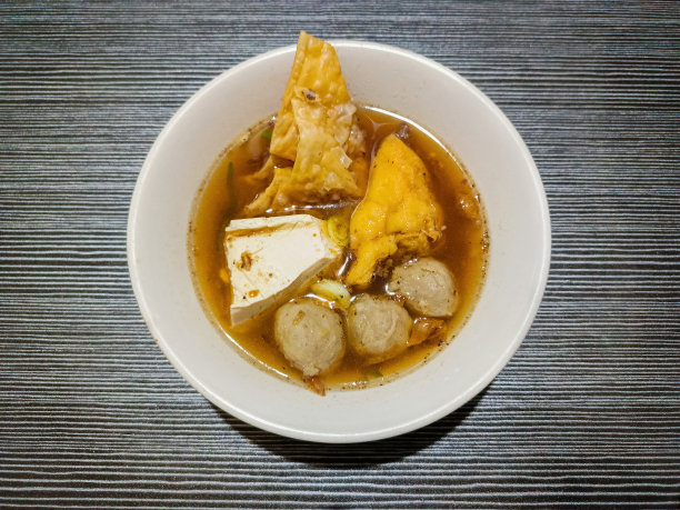 印尼街头小吃“Bakso”，木桌上的白碗里装着肉丸、煮豆腐、炸豆腐和饺子图片下载