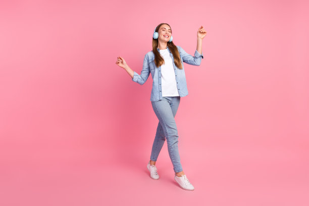 漂亮的年轻女孩的全尺寸照片走路跳舞听音乐耳机穿着时尚的牛仔服装孤立的粉红色背景图片下载