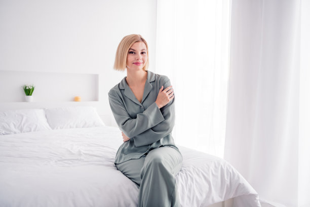 年轻甜美的女士的照片，金发短发模特穿着睡衣广告新室内在卧室拥抱自己隔离在浅白色的房间图片下载