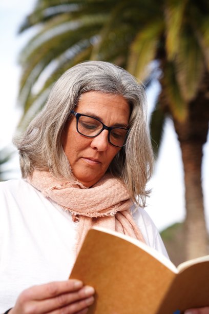 戴着眼镜的白发女人在公园里看书。图片下载