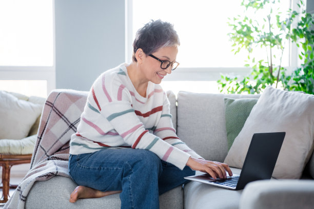 开朗漂亮的女士的照片，坐在舒适的沙发上，使用无线笔记本电脑，在明亮的现代公寓室内共同工作图片下载