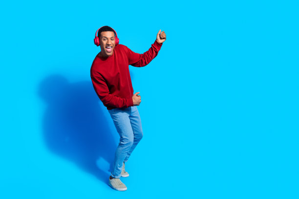 照片积极有趣的男人穿红色时髦的套头衫享受氛围寒冷听音乐无线耳机孤立的蓝色背景图片下载