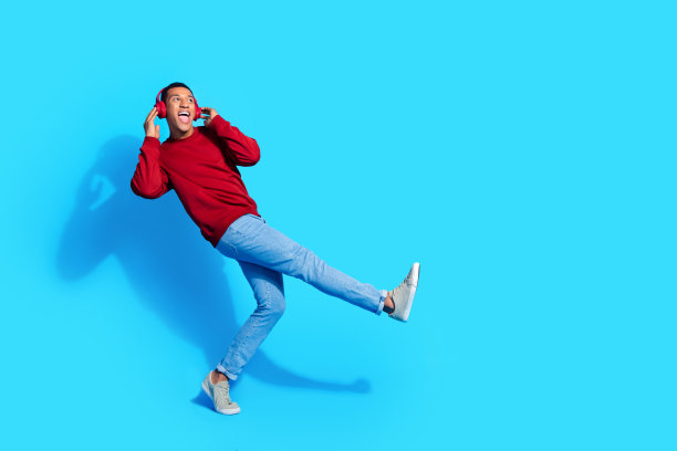 照片上的快乐nice开朗乐观的男人穿着红色时髦的衣服听音乐看起来空旷的空间孤立在蓝色的背景图片下载