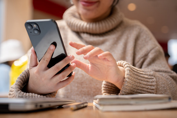 一张裁剪过的照片，一个穿着舒适毛衣的女人坐在咖啡馆的桌子上使用她的智能手机。图片下载