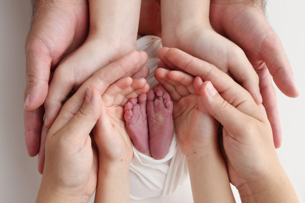 爸爸的手心，妈妈的脚上都抱着刚出生的婴儿的白毯子。新生儿的脚放在父母的手掌上。工作室微距照片的一个孩子的脚趾，脚跟和脚。图片下载