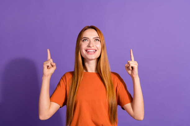 照片的年轻漂亮的女孩在橙色t恤发起人指着上面的广告服装商店孤立的紫色背景图片下载