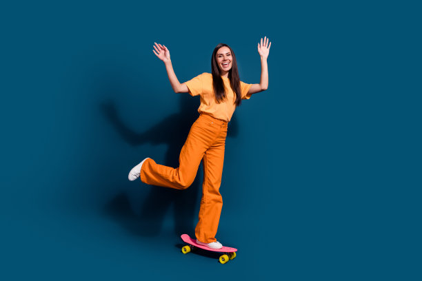 成熟女性的全身照片举起手臂，在深蓝色的背景上骑着粉红色的长板，乐不可支图片下载