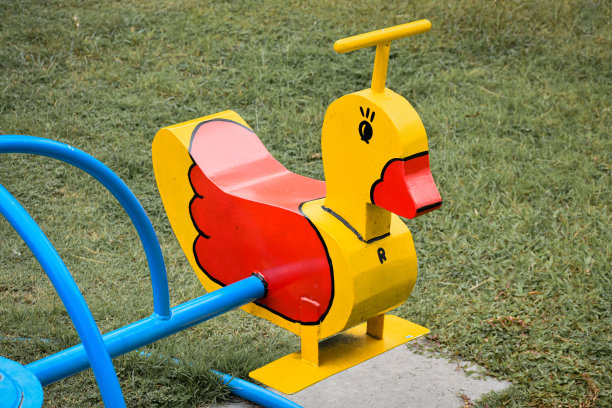 操场上的黄色鸭子形状的旋转木马或儿童旋转木马，背景是绿色的草地。图片下载