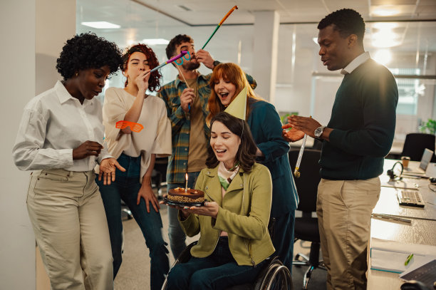 快乐的女商人在工作中用轮椅吹灭蛋糕上的蜡烛图片下载