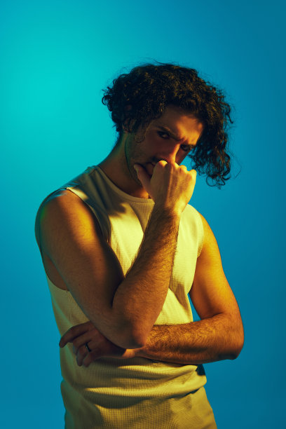 在霓虹灯的蓝色背景下，卷发的年轻人的凝胶肖像，没有刮胡子的脸看着相机，表情严肃图片下载