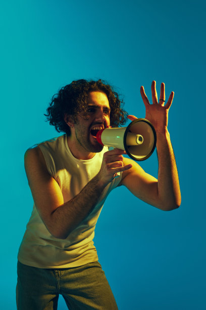 一个情绪化的卷发年轻人，在霓虹灯的蓝色背景下，用扩音器大声喊叫图片下载