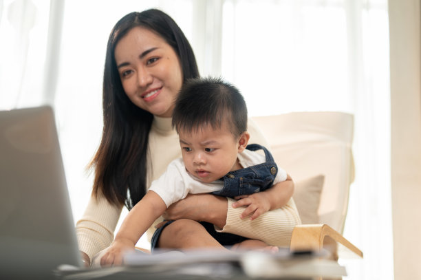 一位美丽的亚洲女商人妈妈在家远程工作，同时照顾她的小儿子。图片下载