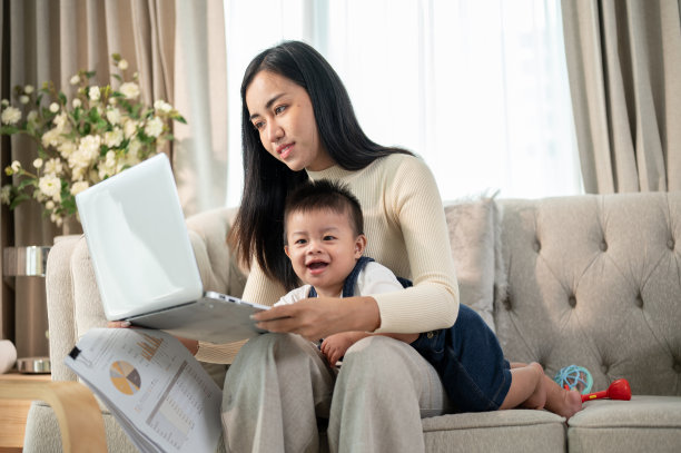 一位快乐的亚洲女商人妈妈在家工作，照顾她淘气的小男孩。图片下载