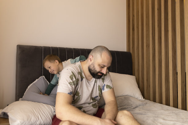 开心的爸爸带着胡子躺在床上和儿子一起在家里玩早上。蓝眼睛穿便服的男孩。父子时刻，亲密的照片图片下载