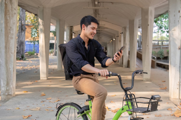 一位年轻的亚洲商人骑着自行车去上班。站在办公室外面打电话，谈生意。减少能源和减少空气污染的理念。图片下载
