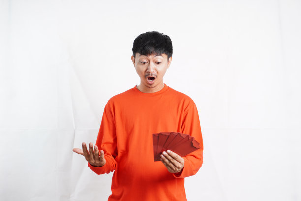 春节快乐。拿着红袍或红包的亚洲男子被隔离在白色背景上。祝你好运、问候和祝贺。有趣的脸图片下载