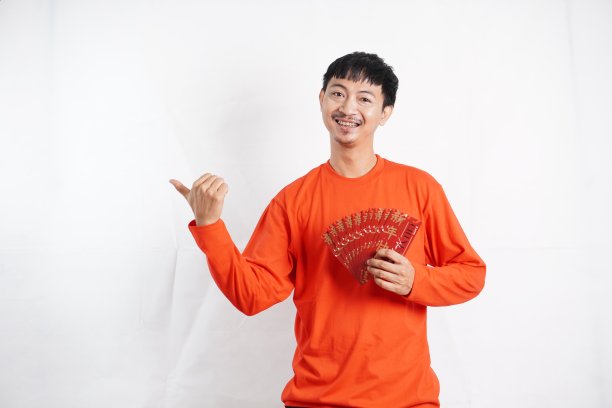 春节快乐。亚洲男子指着并拿着白色背景的红袍或红包。祝你好运、问候和祝贺图片下载