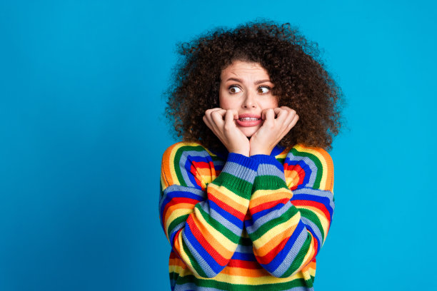 漂亮的年轻女孩的照片肖像紧张咬指甲看起来空的空间穿时髦的彩虹印花服装孤立的蓝色背景图片下载