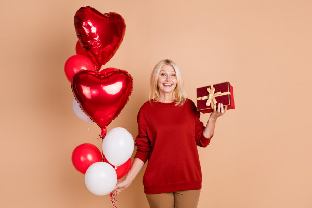 照片的甜美开朗的女士穿着红色套头衫得到礼物气球花束孤立的米色背景图片下载