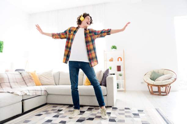 时髦的无忧无虑的家伙穿着格子衬衫，享受歌曲，耳机在室内房间和家里玩得很开心的全长照片图片下载