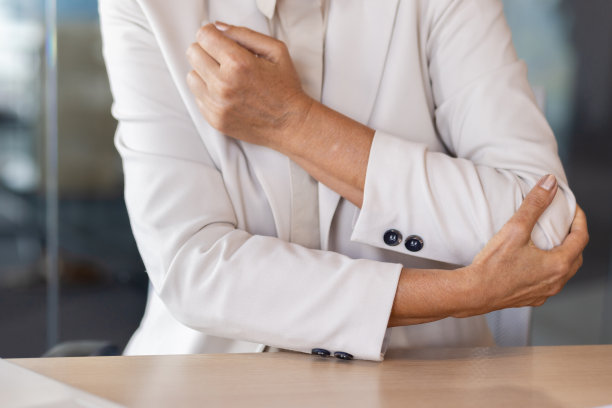 身体某个部位的特写照片。一位身穿米色西装的高级女性坐在办公室的办公桌前，用手托着胳膊肘，感到剧烈的疼痛和痉挛图片下载