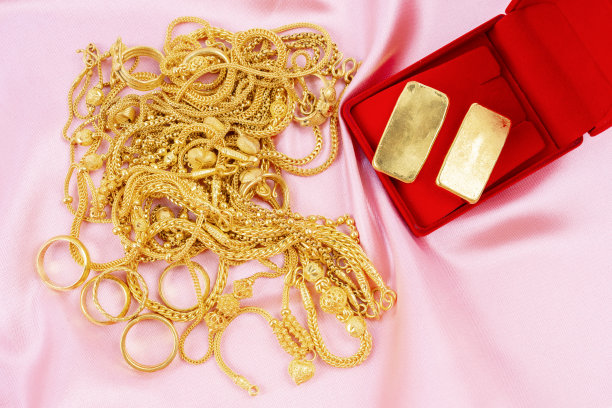 许多金项链和金条放在红色的盒子里，放在粉红色的天鹅绒布上。图片下载