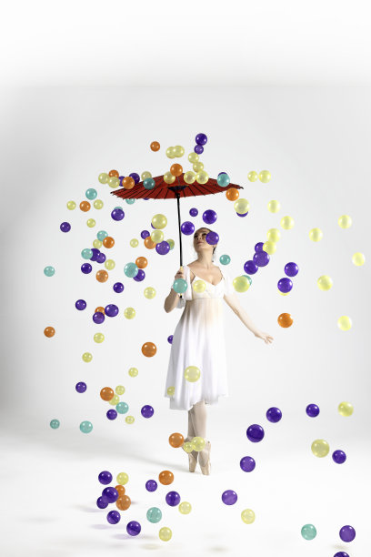 五颜六色的球从天上落下。美丽的芭蕾舞女演员用她的日本伞保护自己免受彩色球的伤害。图片下载