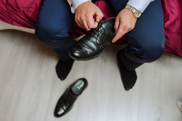 一个优雅的男人穿着黑色的正式皮鞋。把鞋子。商人在地板上系鞋带。新郎正在为婚礼做准备。图片下载