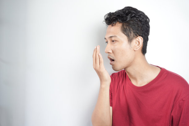 一个男人检查口臭，用手呼吸。口腔和牙齿健康的概念图片下载