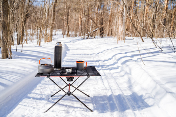 游客的餐桌上站着白雪衬托的桌子，盘子都放在桌子上，在森林里露营。图片下载