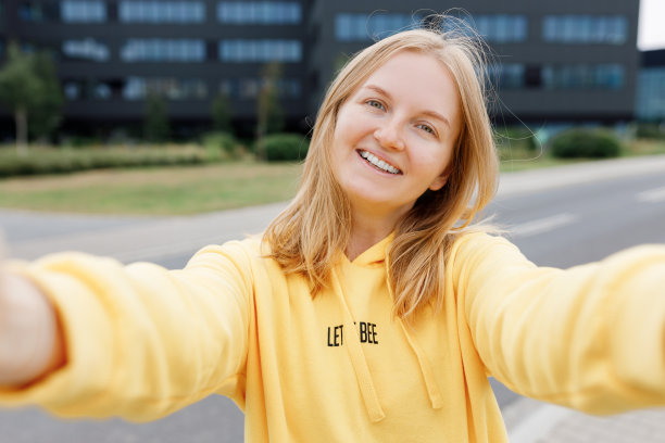 年轻漂亮的女孩说你好。照片轻松迷人积极的女人拿着相机，在现代城市中心户外自拍夏天。生活方式的概念。观点。图片下载