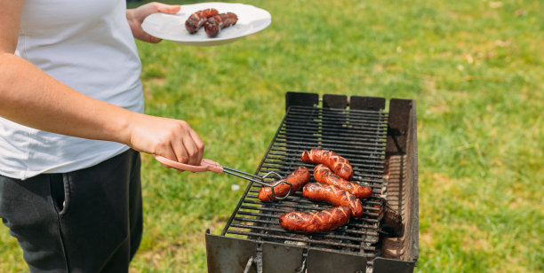在铸铁烤架上烤猪肉香肠。年轻女子的手在烤肉。年轻女性正在烧烤，年轻女孩在家户外准备食物图片下载