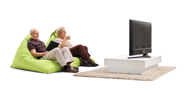 一对上了年纪的男人和女人坐在沙袋上，拿着一杯茶和一本书坐在电视机前图片下载