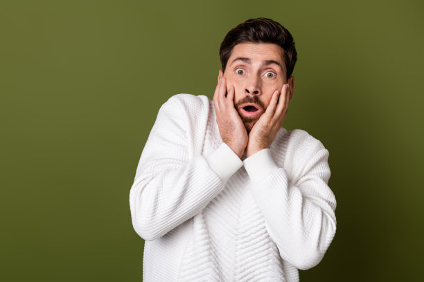 照片中，一名惊恐的男子穿着时髦的衣服，手摸脸颊，omg床上新闻孤立在卡其色背景下图片下载