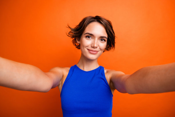 照片的梦幻愉快的女士穿着蓝色背心微笑录制视频视频博客孤立的橙色背景图片下载