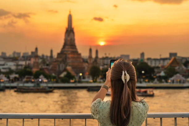 一名女游客在日落时分欣赏着阿仑寺的景色，一名游客在屋顶酒吧用智能手机拍下了黎明寺的照片。曼谷，泰国和东南亚的地标和旅游目的地图片下载