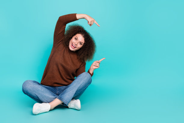 漂亮的年轻女孩的全身照片坐在地板点的空白空间穿着时髦的棕色衣服孤立在海蓝宝石色的背景图片下载