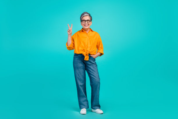 乐观的商务女士的全身照片，成熟的白发模特在蓝色背景的办公室里显示v字图片下载