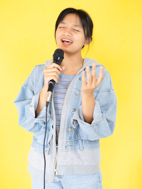 年轻的女孩在黄色的背景上欢快地唱歌跳舞。图片下载