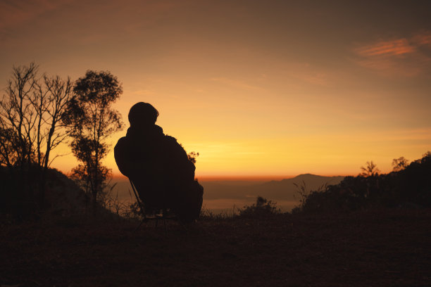 风景和旅行的概念与单独的自由职业者男人坐在椅子上，看日出与山的背景层图片下载