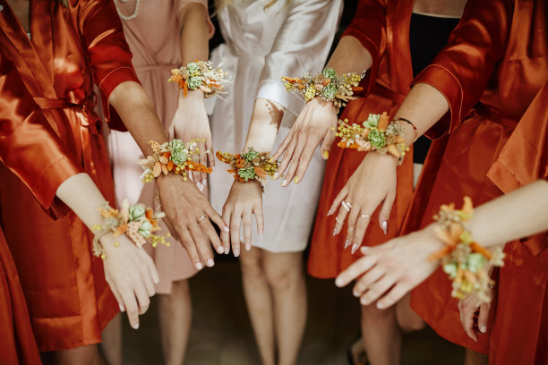 伴娘们穿着橙色的长袍，展示着手腕上的鲜花。库存图片图片下载